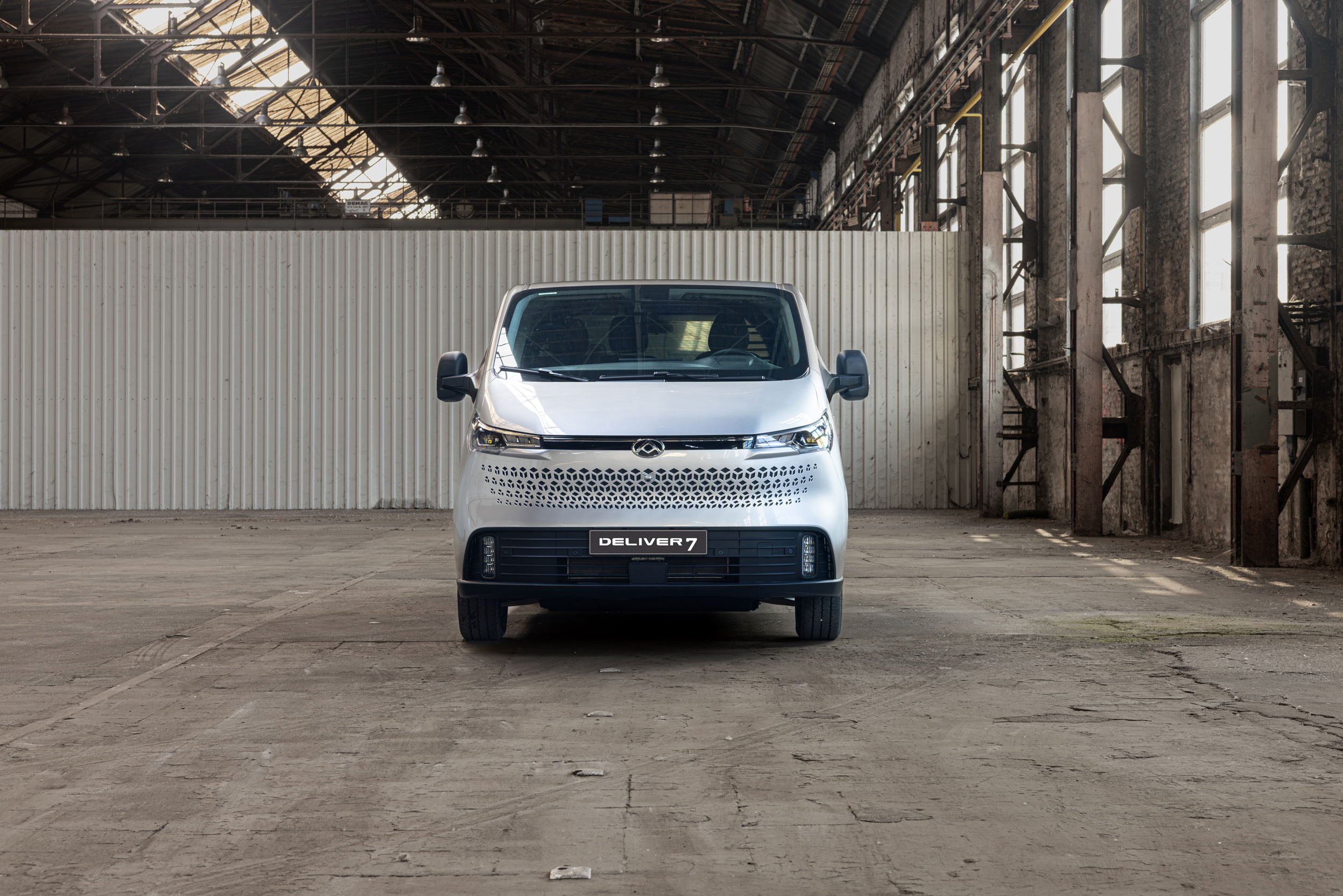 Frontansicht eines silbernen Lieferwagens in einem industriellen Raum mit hohen Decken.