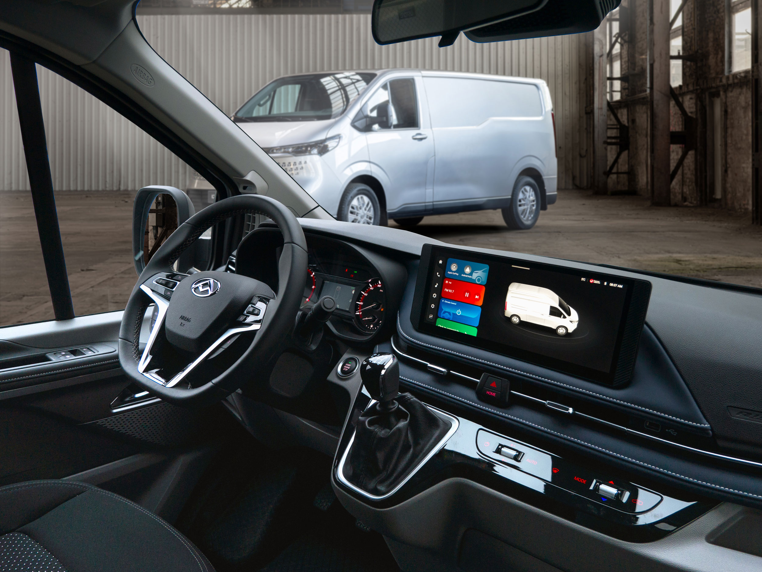 Innenansicht eines Fahrzeugs mit modernem Display, im Hintergrund ein Lieferwagen in einer Industriehalle.