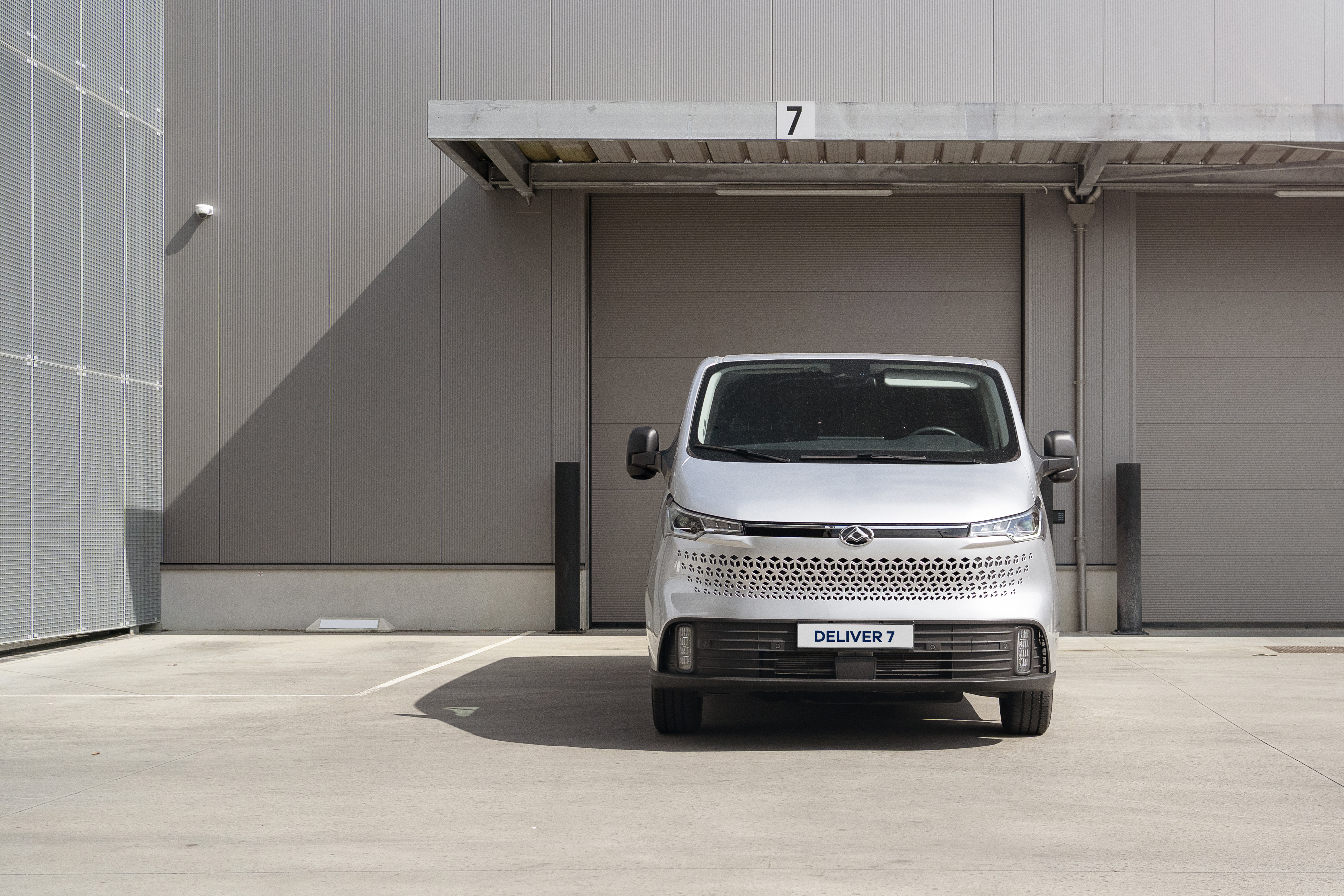 Ein silberner Lieferwagen, Modell DELIVER 7, steht vor einer modernen Lagerhalle.