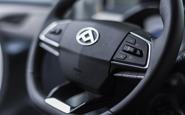 Fokus auf ein modernes Auto-Lenkrad mit Bedienelementen und einem Logo in der Mitte.