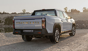 Maxus Pick-up Truck von hinten, mit glänzender Karosserie, steht auf Schotter, umgeben von natürlicher Landschaft.