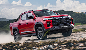 Roter Pickup mit robustem Design, fährt auf unbefestigtem Gelände vor einer malerischen Landschaft.