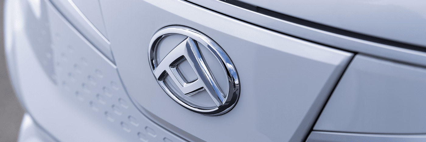 Nahaufnahme des Emblems eines modernen Autos in Silber und Weiß. Das Logo zeigt stilisierte Buchstaben.